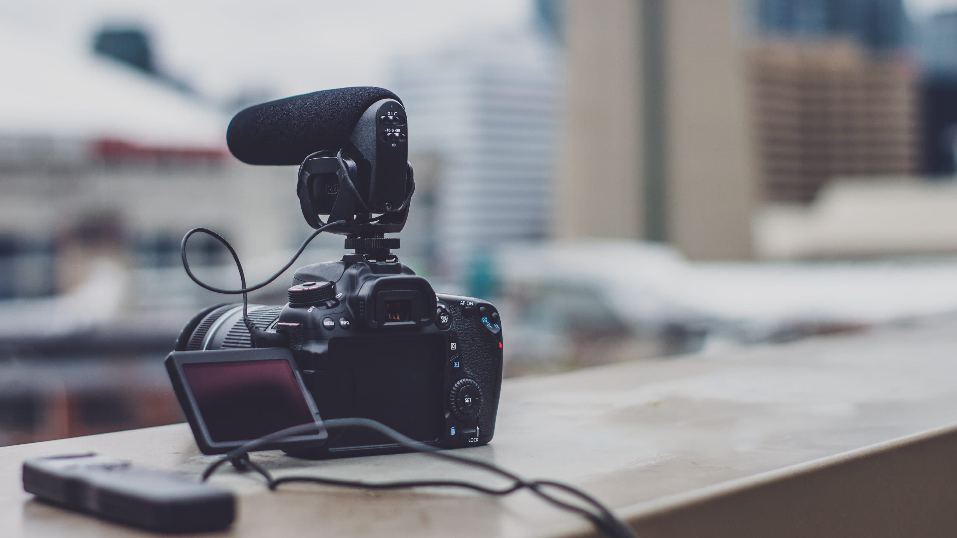 A DSLR fitted with a shotgun microphone, framed against a city skyline.