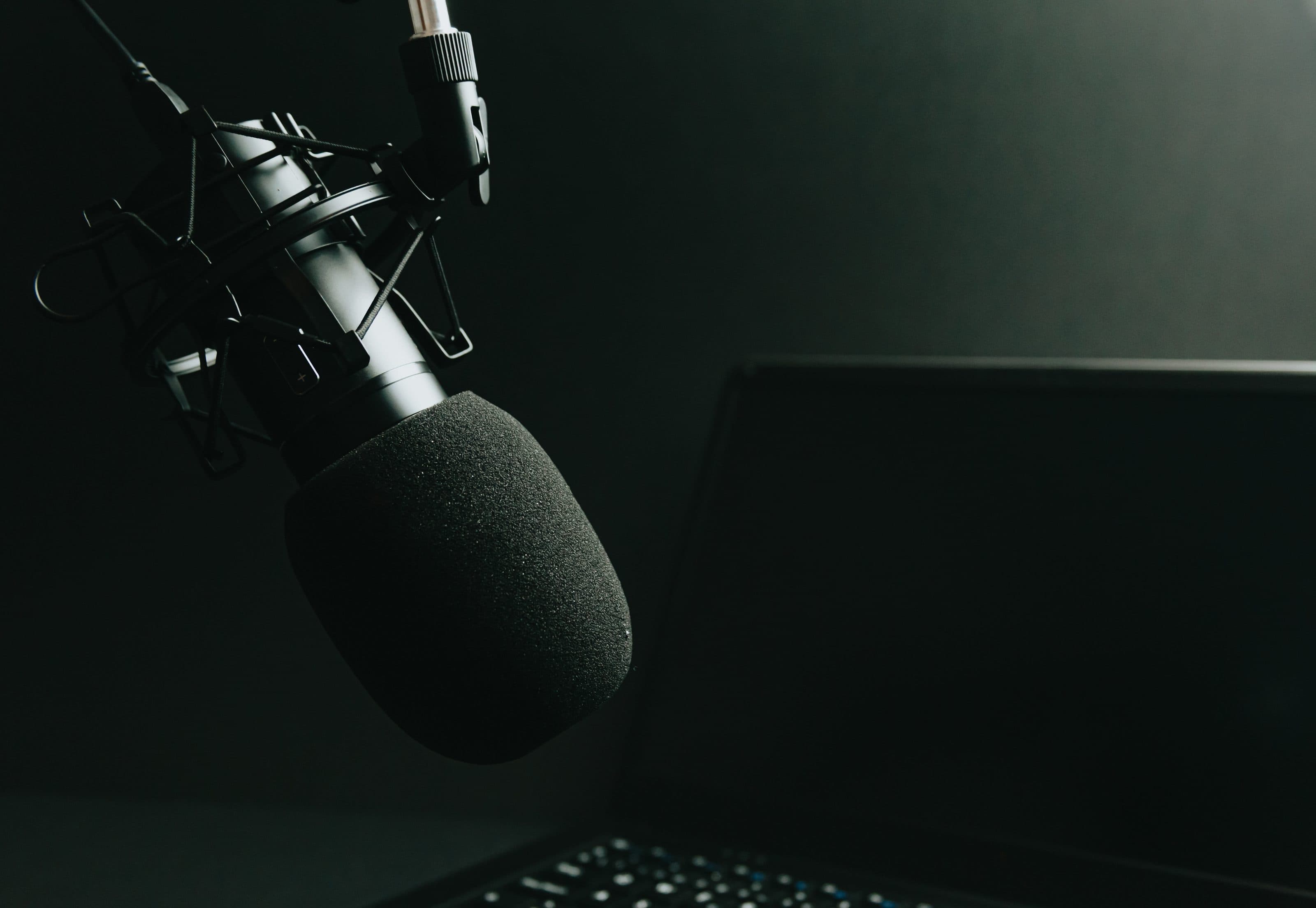 A studio condenser microphone on a boom arm, lit against a dark desk.